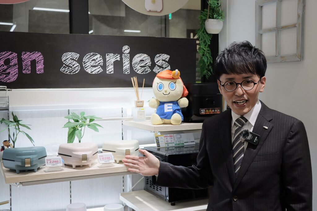 eangleの陳列の前で手を挙げて説明する木村さん